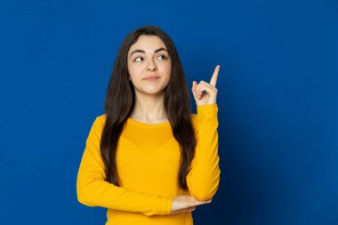 Esmer genç kız mavi arka planda sarı forma giyiyor.