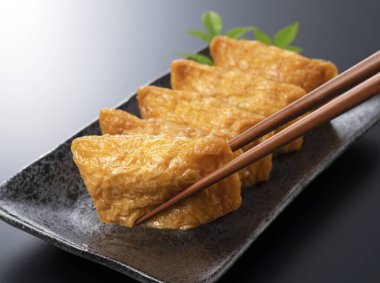 Japon Inari Sushi 'si siyah bir zemine karşı siyah bir tabakta yemek çubuklarıyla kaldırılır.