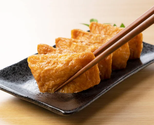 Japanese Inari Sushi Black Plate Set Wooden Background Lifted Chopsticks — Stock Photo, Image