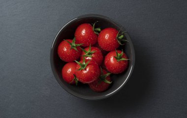 Siyah arka planda bir kasede domateslerin kuş bakışı görüntüsü.