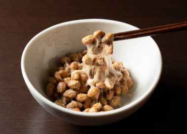 Koyu ahşap arka planda duran tabakta duran Natto yemek çubuklarıyla kaldırılır..