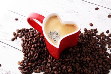 Kırmızı kalp kahve fincanı ve fasulye masada.
