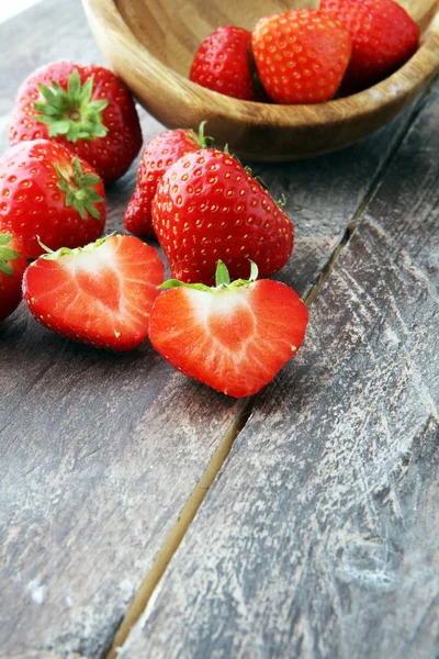 Fresh strawberries in a bowl and on a wooden background — Stock Photo, Image
