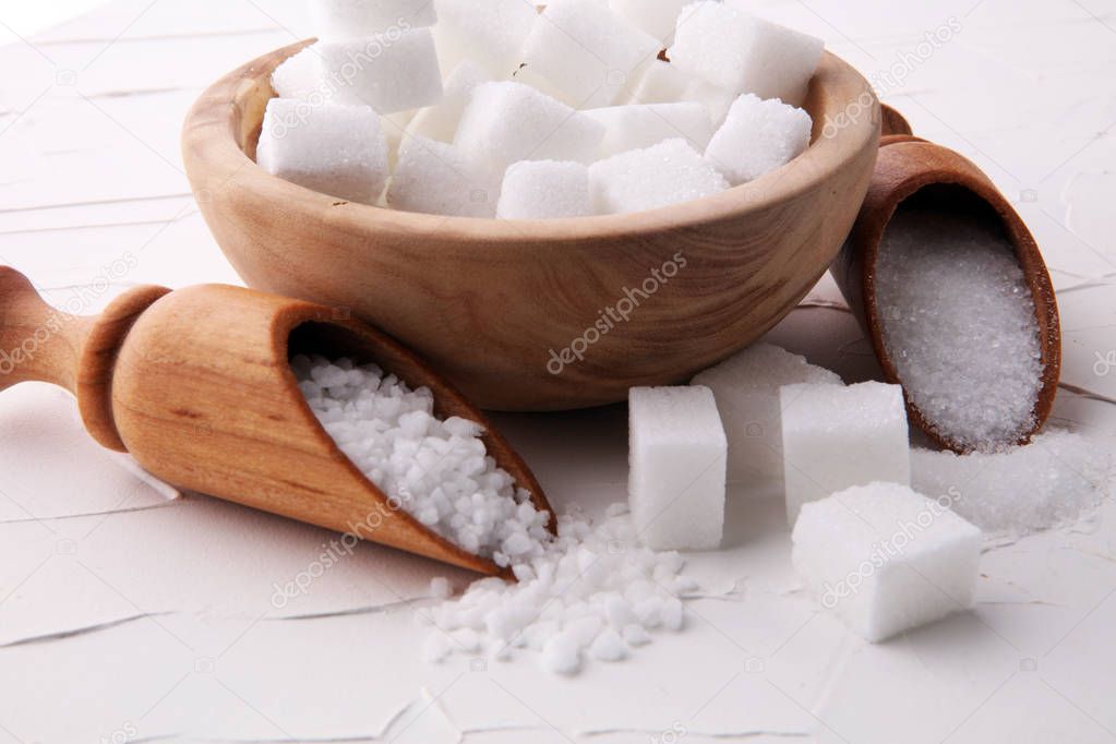 Close up the sugar cubes and cane in wooden spoon on the table 