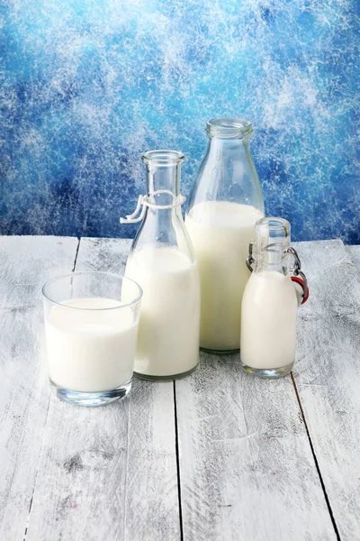 A jug of milk and glass of milk on a wooden table.