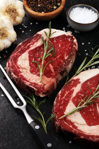 Surowe świeże mięso Ribeye Steak, przyprawy i widelec do mięsa na rustykalnym b — Zdjęcie stockowe