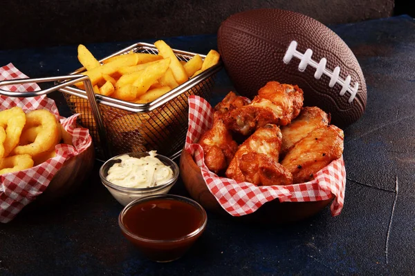 Skrzydełka kurczaka, frytki i pierścienie cebulowe do piłki nożnej na stole. Gr — Zdjęcie stockowe