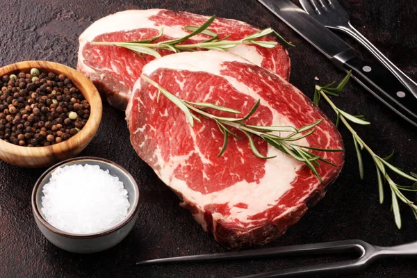 Carne fresca cruda Ribeye Filete, condimento y tenedor de carne en rústico b — Foto de Stock