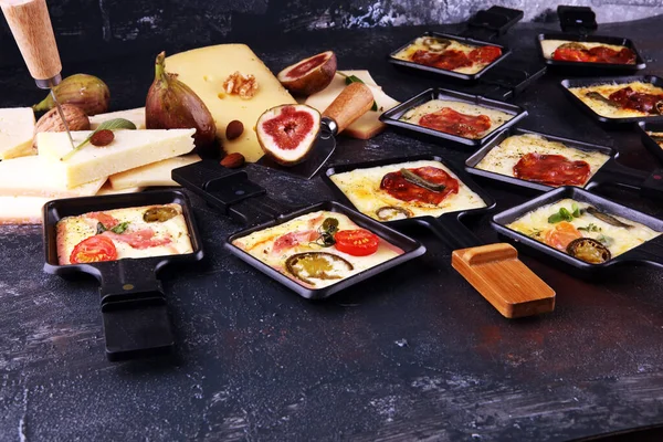 Delicious traditional Swiss melted raclette cheese on diced boiled or baked potato served in individual skillets with salami and potatoes