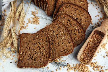 Kesme tahtasında dilimlenmiş çavdar ekmeği. Köy arka planında tohumlu tam tahıllı çavdar ekmeği.