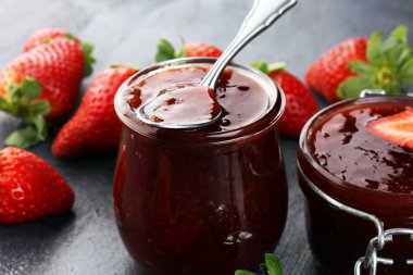 Çilek reçeli cam kavanozda, çilekli ve yapraklı. Ev yapımı çilekli marmelat ve meyve.