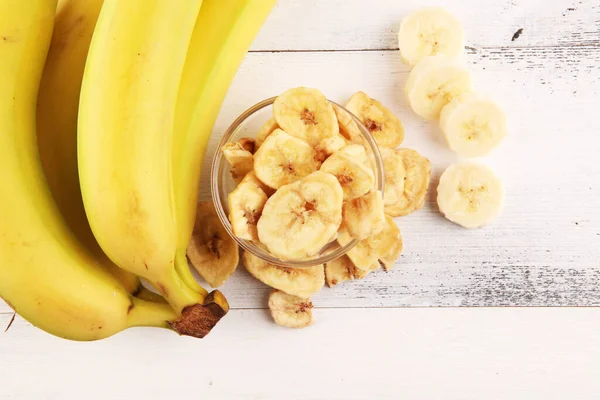 Homemade Dehydrated Banana Chips in a Bowl and fresh banana and slices on table