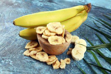 Ev yapımı kurutulmuş muz cipsi kasede taze muz ve dilimler masada.