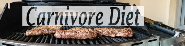 The word Carnivore diet on a panorama of a barbeque with steaks on it. Concept of the controversial diet