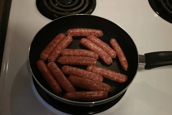 Fried sausages on a frying pan on a wooden background — Stock Photo, Image