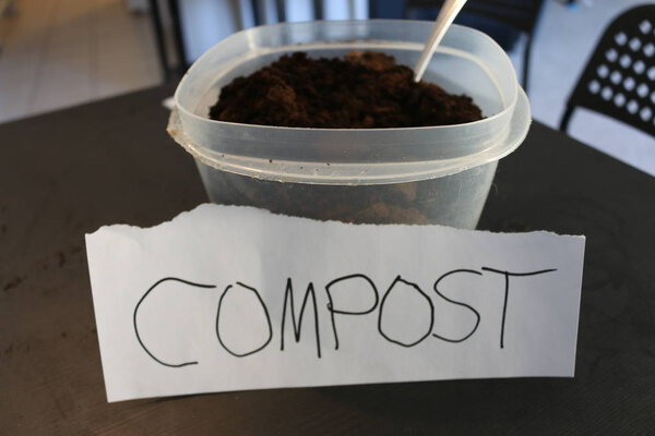 Photo of a container of used coffee grounds with a sign that says compost