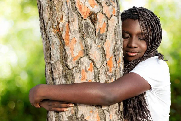 Afrikaanse jongere met vlechten omarmen boom. — Stockfoto