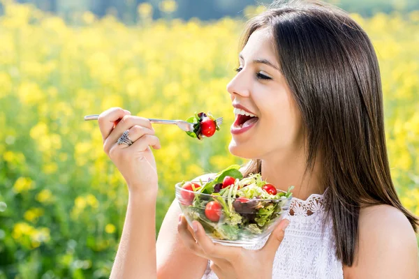 Chica sana comiendo ensalada al aire libre con campo de flores en backgrou — Foto de Stock