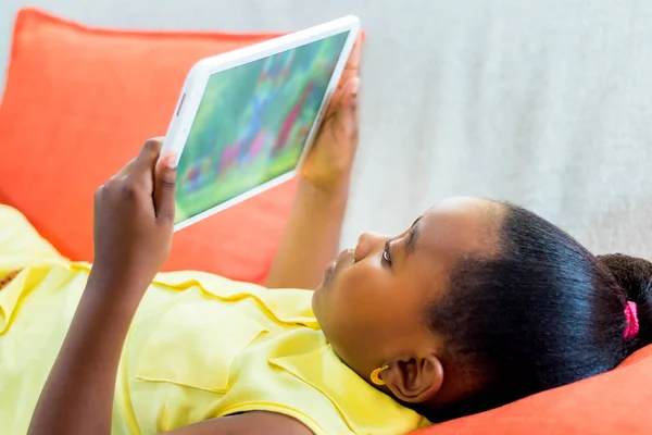 Pequena menina africana assistindo desenhos animados em casa em tablet . — Fotografia de Stock
