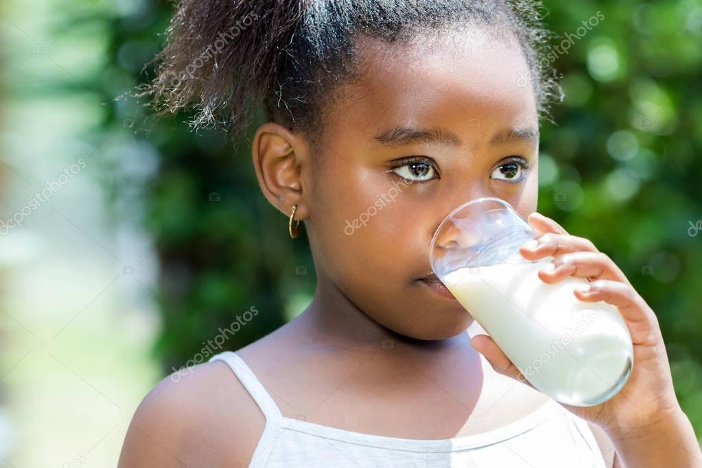 Little african girl drinking milk outdoors.