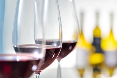 Makro, arka planda odak şarap şişeleri olmayan üç kırmızı şarap bardağını kapat..