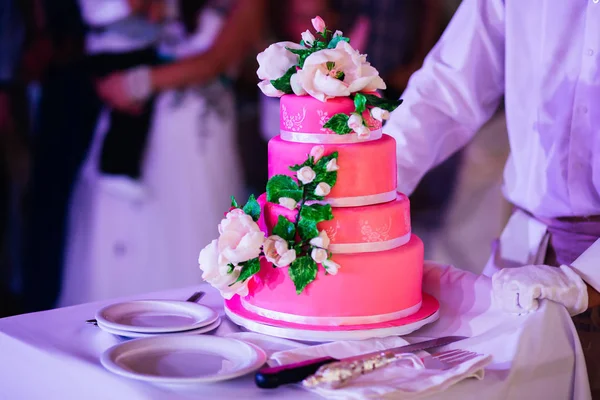 Waiter in white gloves carrying pink wedding cake decorated