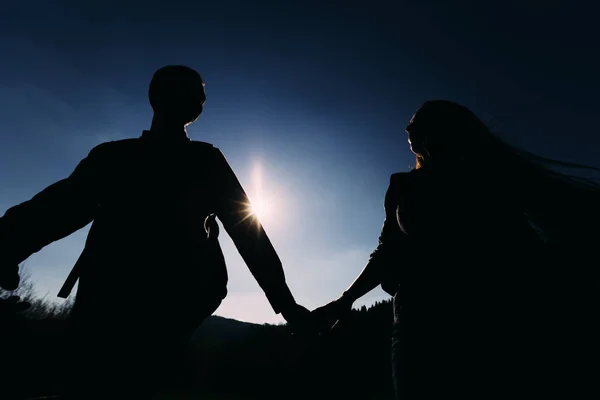 Σιλουέτες των ζευγάρι κρατώντας τα χέρια με ήλιος λάμπει — Φωτογραφία Αρχείου