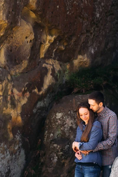 Beautiful couple wearing casual shirts stand at rock