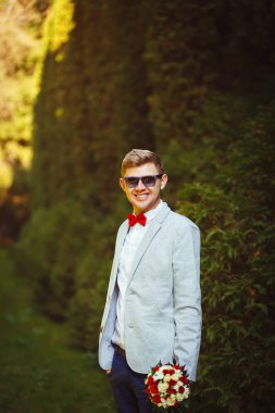 Güneş gözlüğü ve kırmızı papyon sonbahar parkta gülümseyen güneşli günde neşeli genç adam