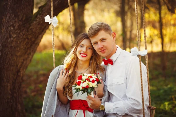 Krásná blonďatá pár podívat na kameru na houpačce v podzimní park — Stock fotografie