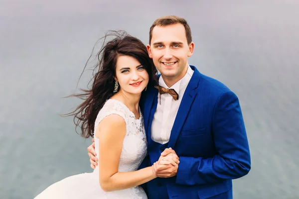 Cheerful wedding couple looks happy hugging at the camera. Groom