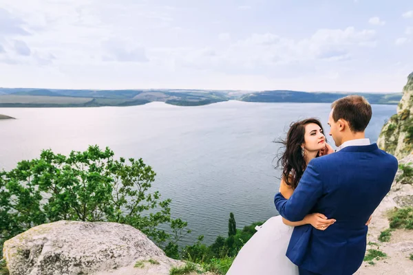 Belo casal de pé sobre a rocha acima do lago e olhando — Fotografia de Stock