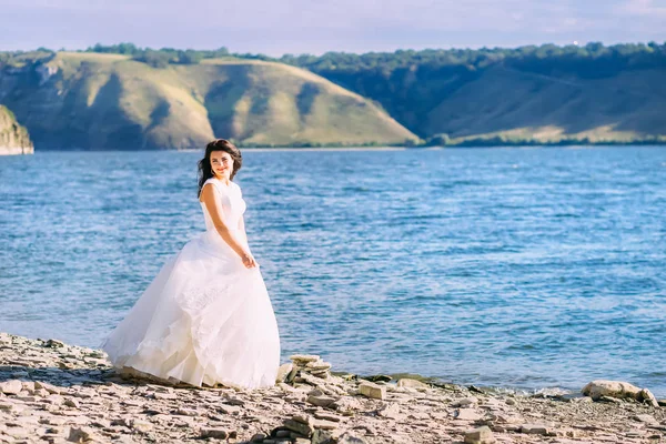 Noiva encantadora em vestido branco andando à beira de um lago — Fotografia de Stock