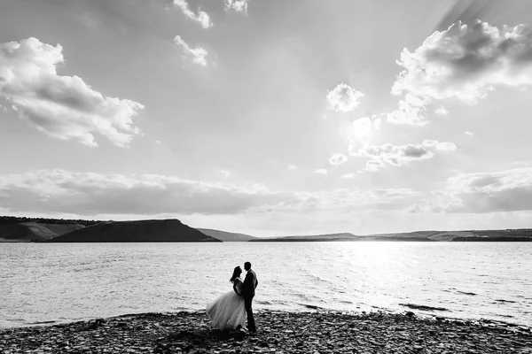 Bonita pareja de boda de pie en la orilla de piedra de un lago con f — Foto de Stock