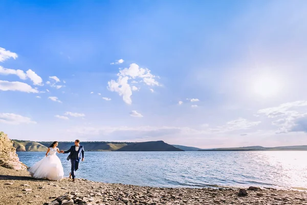 Hermosa pareja de boda caminando por la costa de un lago pintoresco — Foto de Stock