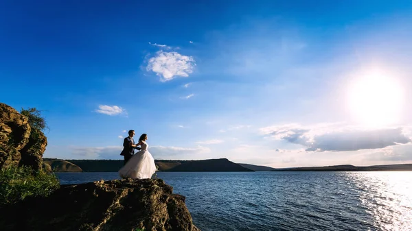 Όμορφο γαμήλιο ζεύγος στέκεται πάνω στο βράχο με ήρεμη θάλασσα και — Φωτογραφία Αρχείου