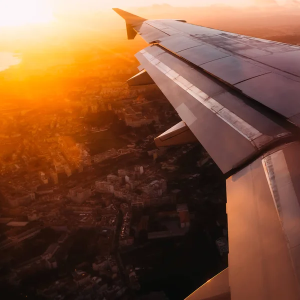 Αεροπλάνο πτέρυγα σε φόντο από μεγάλη πόλη σε ακτίνες ηλιοβασίλεμα — Φωτογραφία Αρχείου
