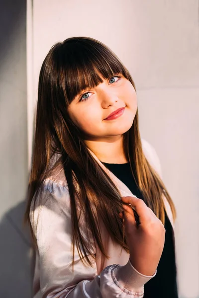 Beautiful little girl holding tips of her hair and staring at th