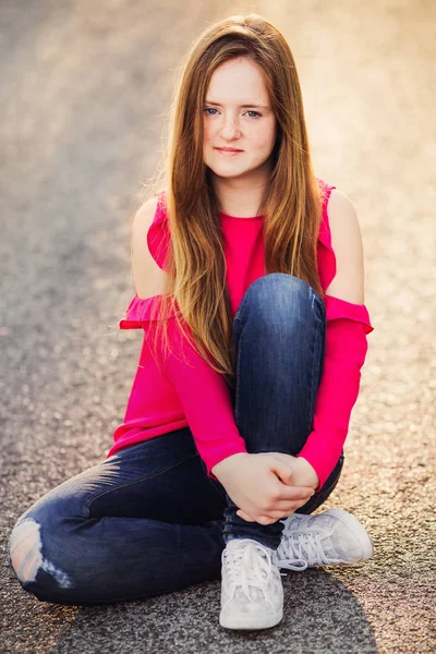Adolescente sola sentada en el asfalto sosteniendo su rodilla — Foto de Stock