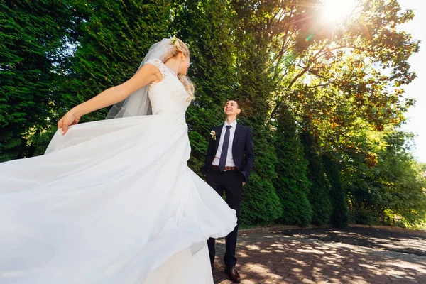Невеста кружится перед мужем в солнечный день в парке — стоковое фото