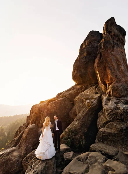 Groom regarde sa femme tout en se tenant debout sur la haute énorme roche — Photo