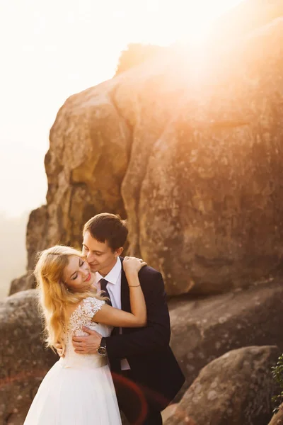 Le soleil du soir illumine les rochers où le couple de mariage s'embrasse — Photo