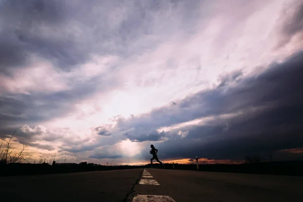 Mädchensilhouette läuft in Sportbekleidung mit großen Wolken in der — Stockfoto