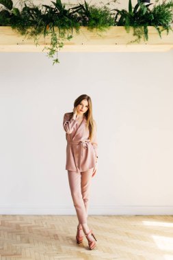 Yeşil plantati ile beyaz duvarının yakınında duran ince zarif kadın