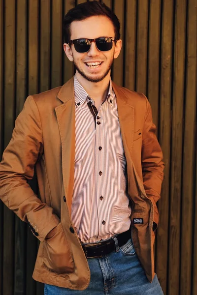 Sonriente hombre elegante con chaqueta marrón y gafas de sol sostiene hi —  Fotos de Stock