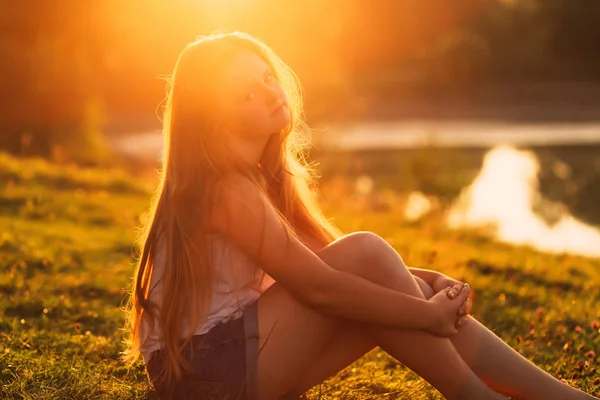 Красива молода дівчина з довгим волоссям сидить на траві в авто — стокове фото