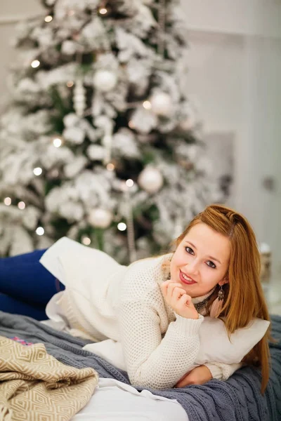 Ragazza sdraiata sul letto contro l'albero di Natale sfocato — Foto Stock