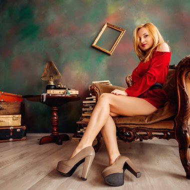 Yüksek moda modeli yüksek topuklu ve armcha içinde oturan kırmızı elbise