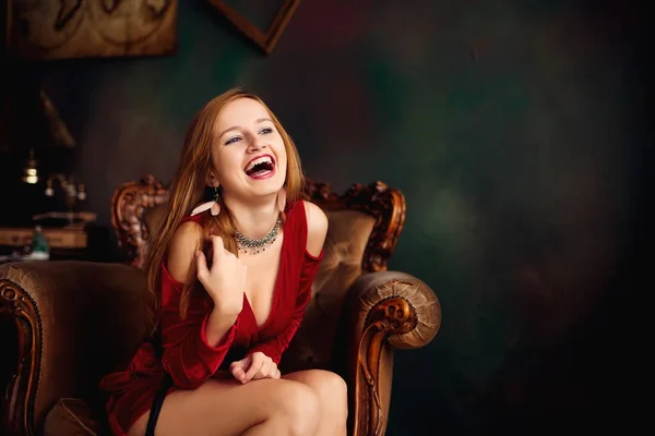 빨간 드레스에 아름 다운 행복 한 여자는 명품에 앉아있는 동안 웃음 — 스톡 사진