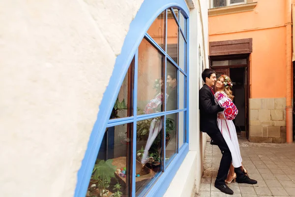 Wunderschöne Hochzeitspaar genießt einen sonnigen Tag in der Nähe eines blauen Fensters wi — Stockfoto